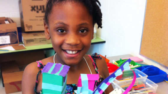 A young girl poses with her project from Architecture Explorations